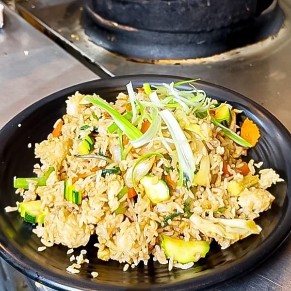 Thai fried rice with zucchini, carrots, and green onions on a black plate.