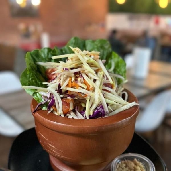 Thai papaya salad with shredded vegetables and lettuce in a rustic brown bowl.