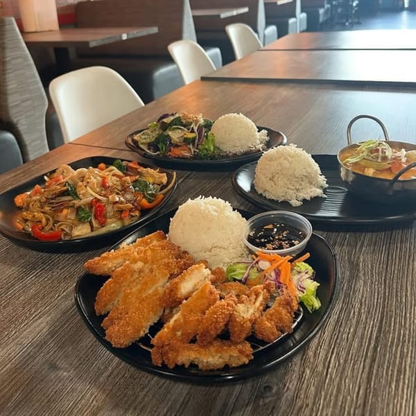 A table laden with various Thai dishes, including fried chicken, noodles, curry, and rice.