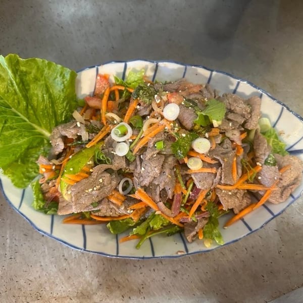 Thai beef salad with lettuce, carrots, onions, and herbs in a striped bowl.