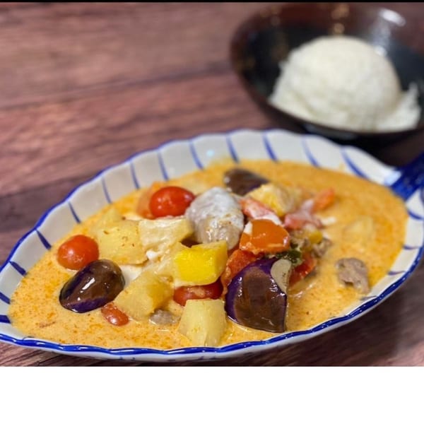 Thai red curry with vegetables and meat, served in a leaf-shaped dish with a side of rice.