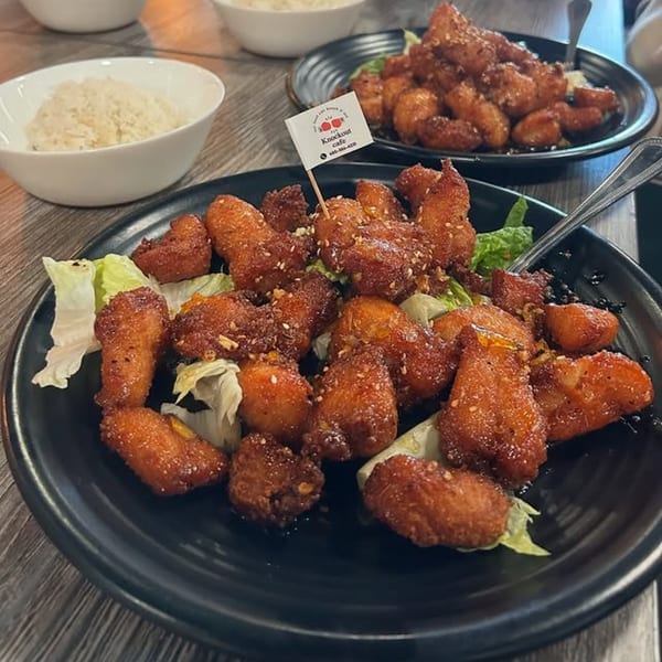 Two plates of crispy Thai fried chicken with sesame seeds and lettuce, with rice bowls in the background.