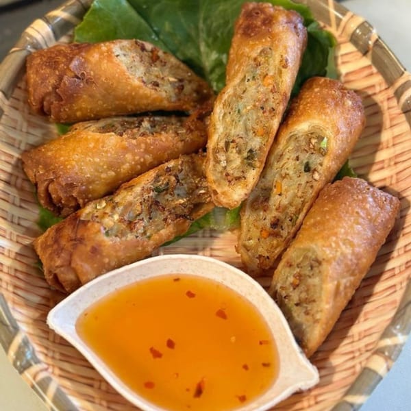 Crispy Thai spring rolls with sweet chili dipping sauce, served in a woven basket.