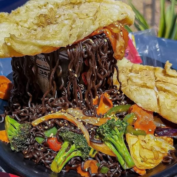 Black noodles with broccoli, carrots, and other vegetables, topped with crispy fried wontons.